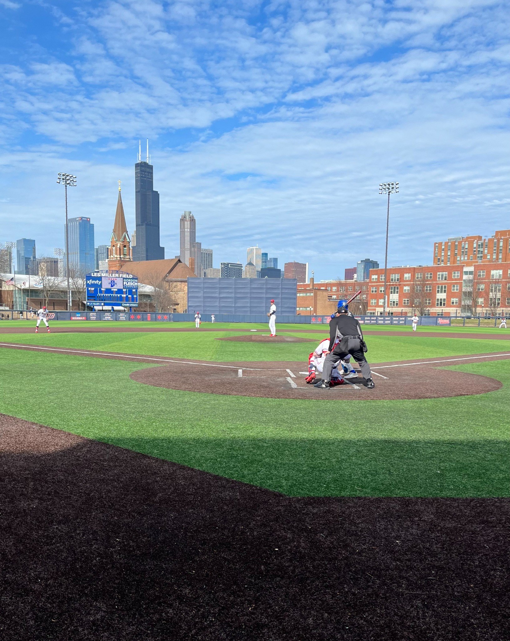 College baseball game from behind home plate with Chicago skyline